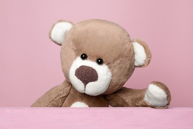 Photo of Cute teddy bear behind wooden plank on pink background
