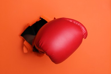 Photo of Man breaking through orange paper with boxing glove, closeup