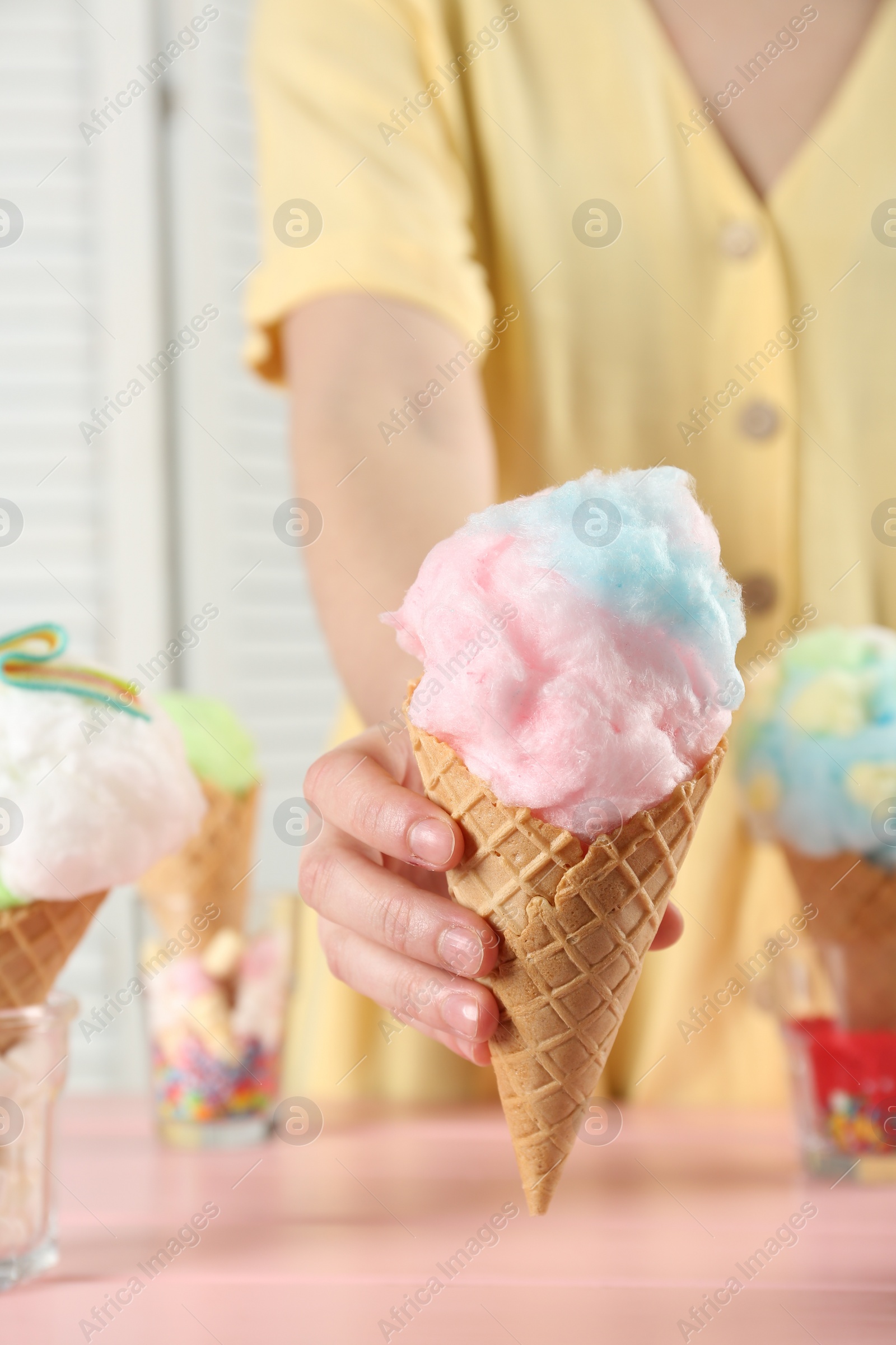 Photo of Woman holding waffle cone with cotton candy indoors, closeup