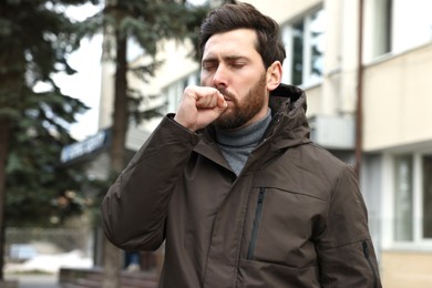 Photo of Sick man coughing on city street. Cold symptoms