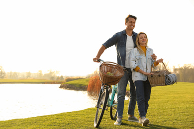 Photo of Young couple with bicycle and picnic basket near lake on sunny day