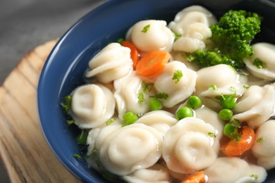 Bowl of tasty dumplings in broth on table, closeup