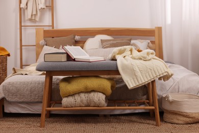 Large comfortable bed with soft sweaters, pillows and blanket in room. Home textile