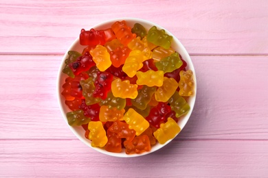 Photo of Bowl with delicious bright jelly bears on pink wooden table, top view