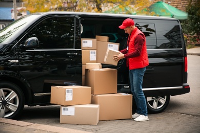 Courier with parcels near delivery van outdoors