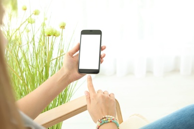 Woman holding smartphone with blank screen on blurred background. Mockup for design