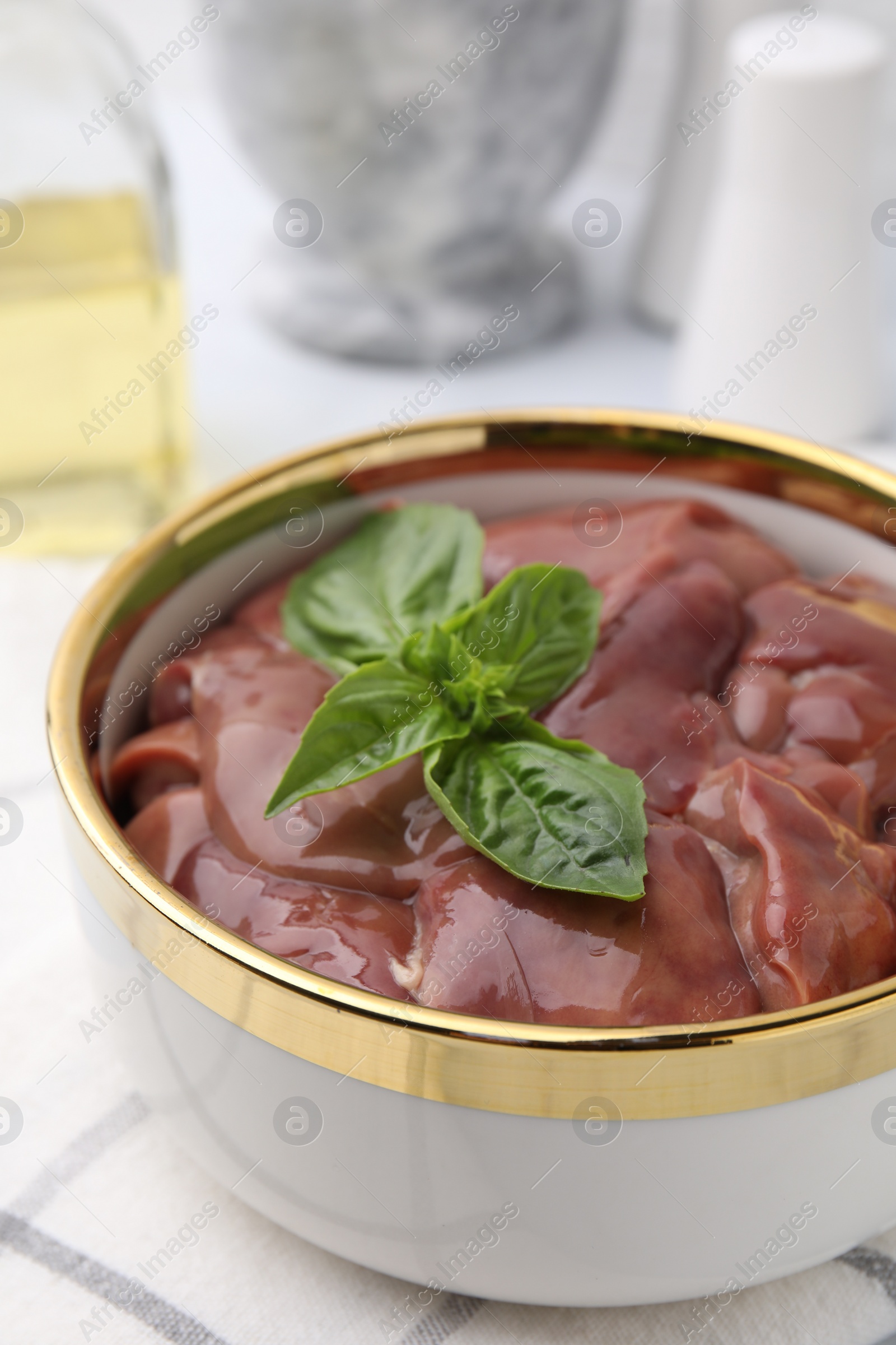 Photo of Bowl with raw chicken liver and basil on table, closeup