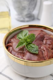 Bowl with raw chicken liver and basil on table, closeup