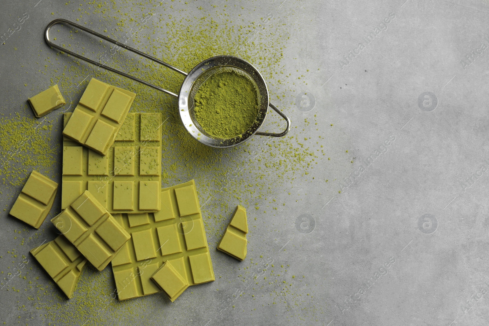 Photo of Pieces of tasty matcha chocolate bars and powder on grey textured table, flat lay. Space for text