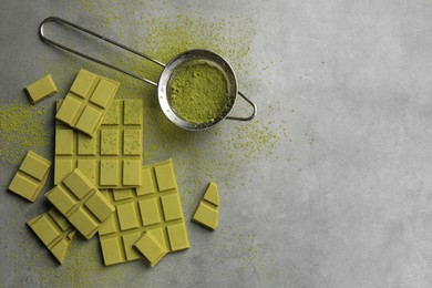 Pieces of tasty matcha chocolate bars and powder on grey textured table, flat lay. Space for text