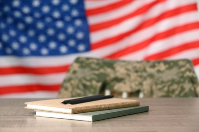 Photo of Notebooks and pencils on wooden table against flag of USA. Military education