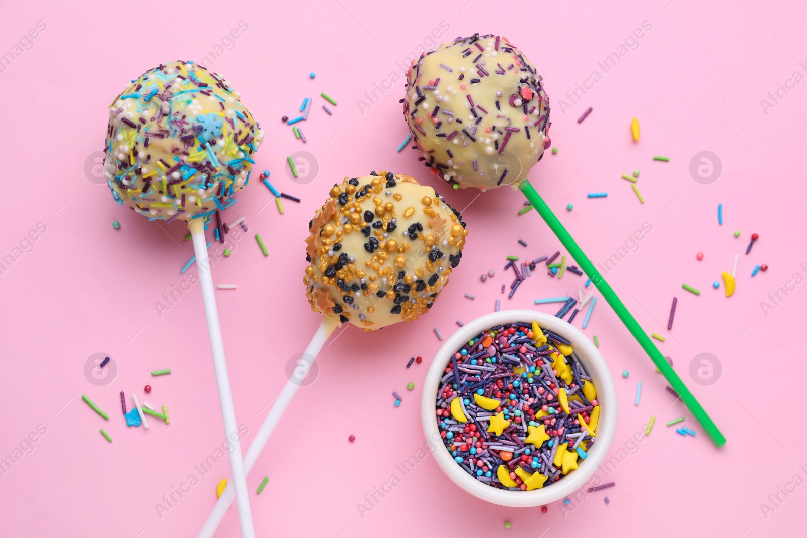 Photo of Delicious confectionery. Sweet cake pops and sprinkles on pale pink background, flat lay