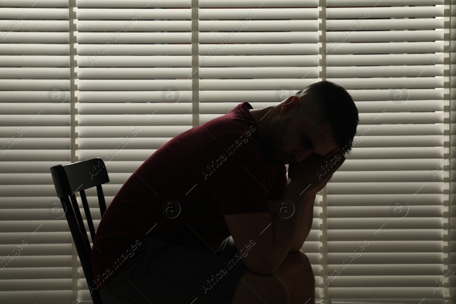 Photo of Sad man sitting near closed blinds indoors