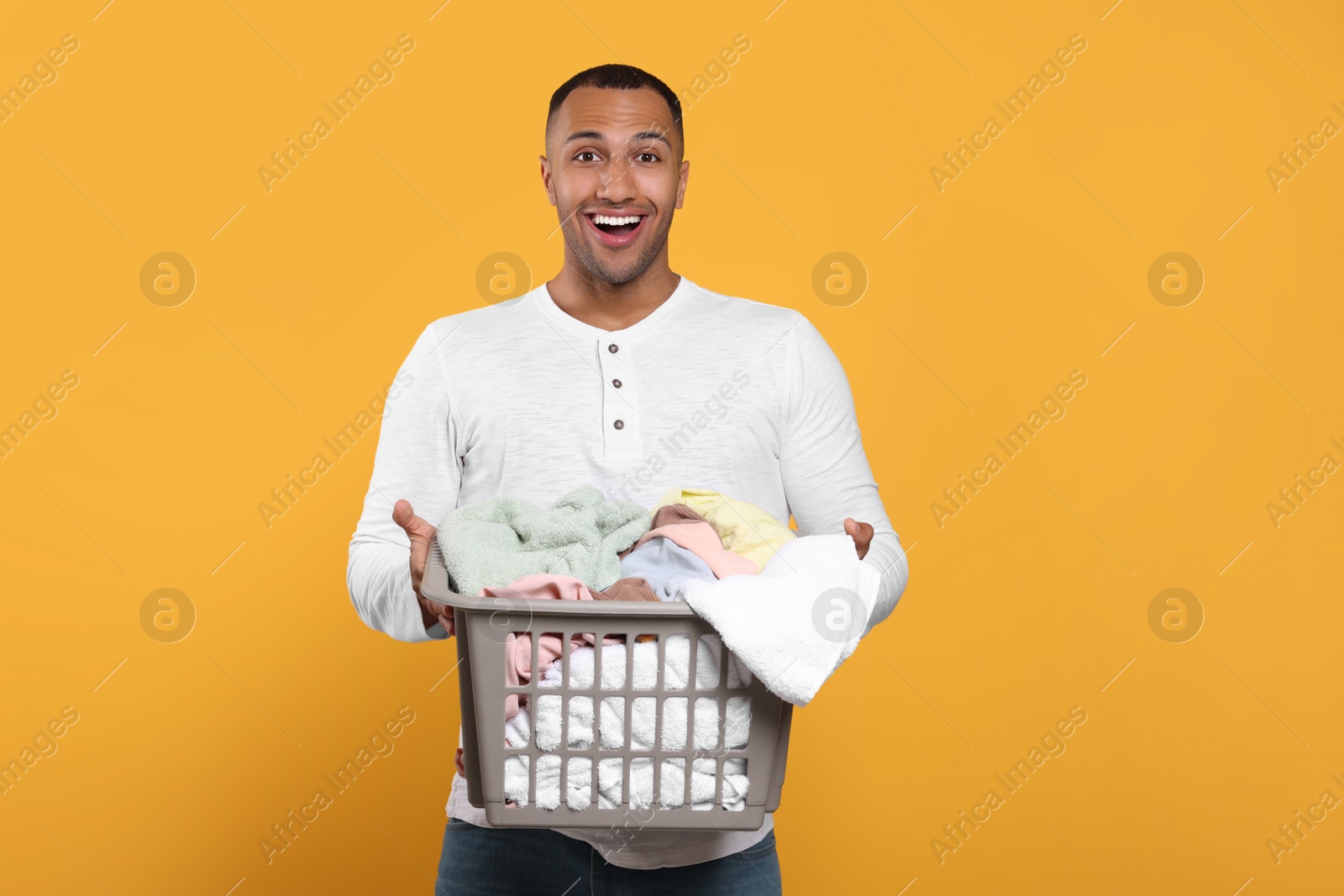 Photo of Emotional man with basket full of laundry on orange background