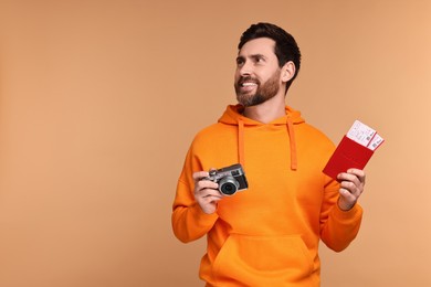 Smiling man with passport, camera and tickets on beige background. Space for text