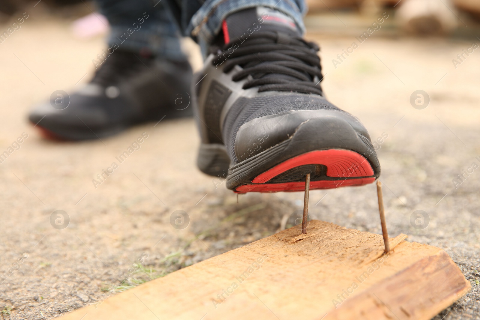 Photo of Careless worker stepping on nails in wooden plank outdoors, closeup