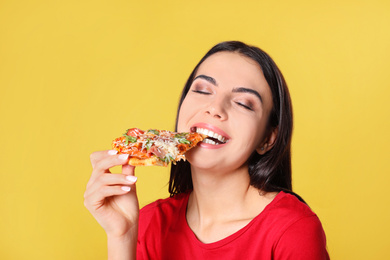 Photo of Beautiful woman eating tasty pizza on yellow background