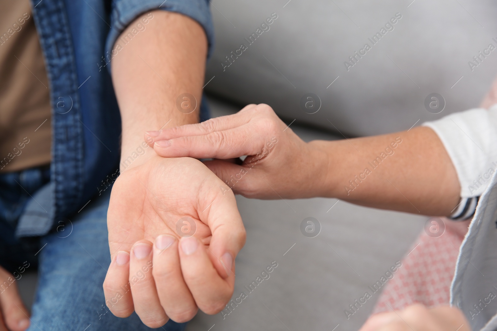 Photo of Mature woman checking man's pulse with fingers indoors, closeup