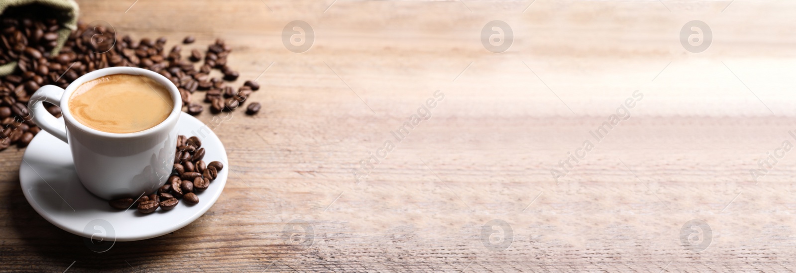 Photo of Cup of hot aromatic coffee and roasted beans on wooden table. Space for text