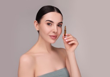 Beautiful young woman holding skincare ampoule on grey background