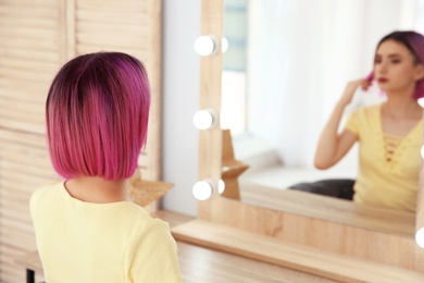 Photo of Young woman with color hair looking into mirror in beauty salon. Modern trend