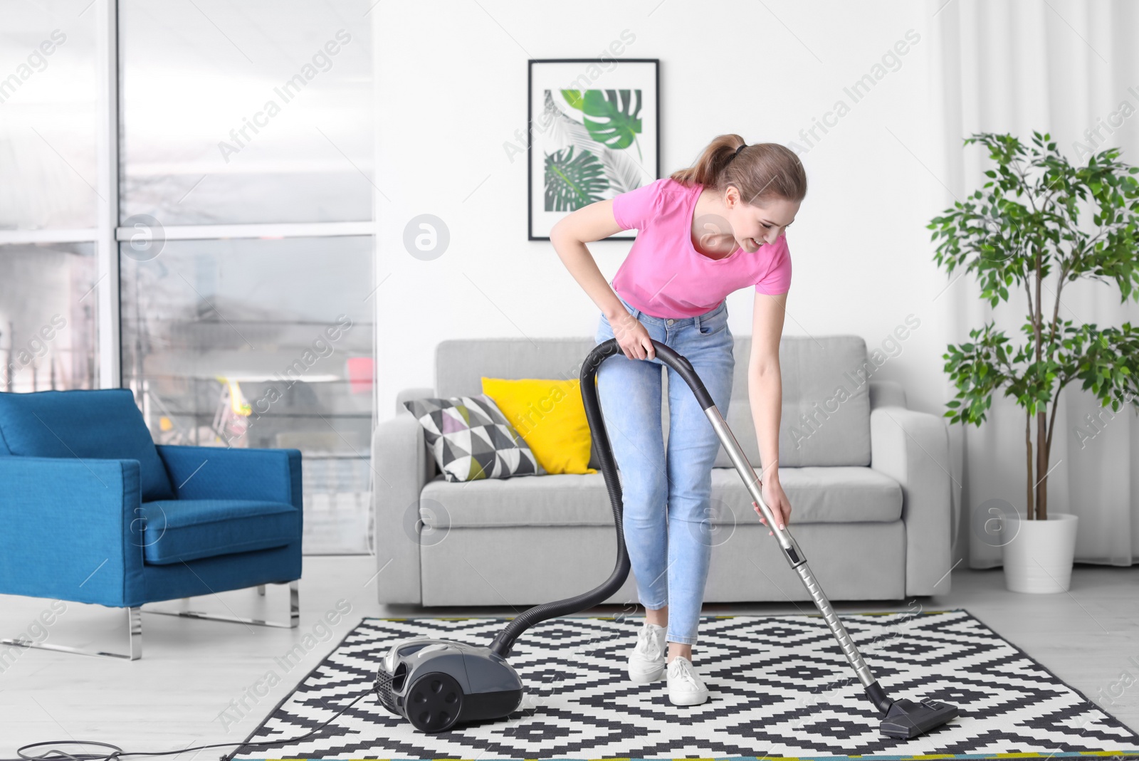 Photo of Young woman hoovering carpet at home