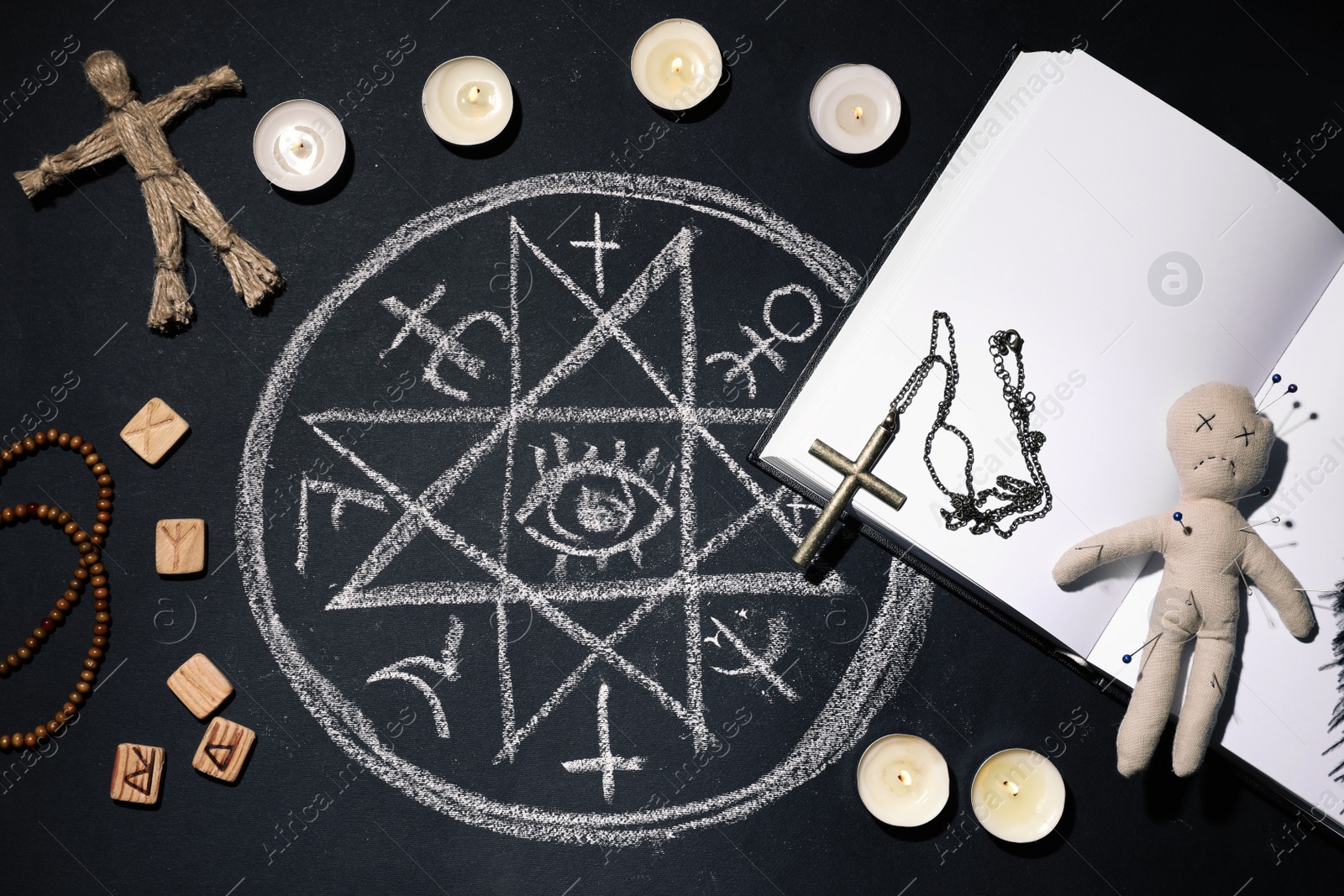 Photo of Voodoo doll with pins surrounded by ceremonial items on black table, flat lay