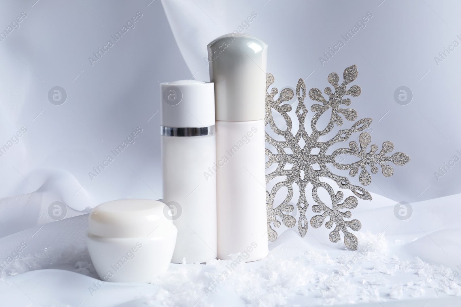 Photo of Set of cosmetic products and decorative snow on white fabric. Winter care