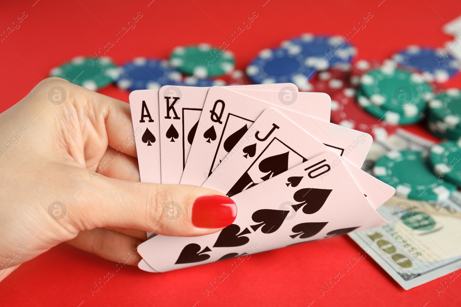 Photo of Woman holding playing cards with royal flush combination at red table, closeup