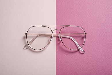 Stylish pair of glasses with metal frame on color background, top view
