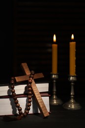 Church candles, Bible, rosary beads and cross on wooden table