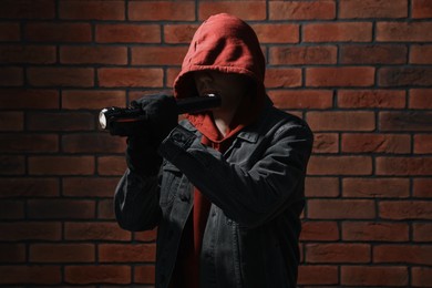 Thief in hoodie with flashlight against red brick wall