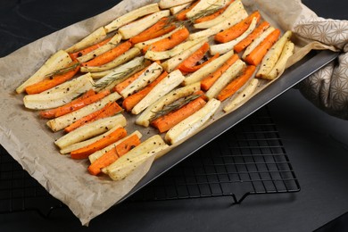 Tray with parchment, baked parsnips and carrots on black table