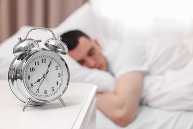 Man sleeping in bedroom, focus on alarm clock. Space for text