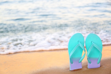 Photo of Stylish flip flops on sand near sea, space for text. Beach accessories