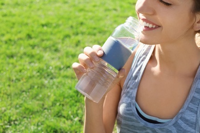 Photo of Young woman drinking clean water from bottle outdoors, closeup. Space for text