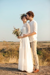 Photo of Happy newlyweds with beautiful field bouquet outdoors