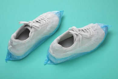 Photo of Sneakers in shoe covers on turquoise background, closeup