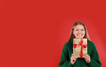 Happy young woman with Christmas gift on red background. Space for text