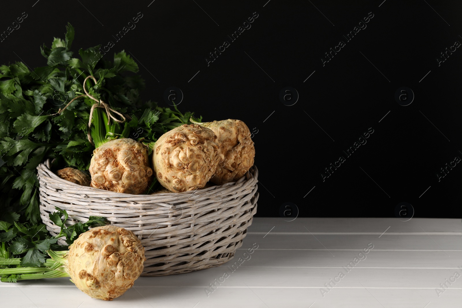 Photo of Fresh raw celery roots in wicker basket on white wooden table. Space for text