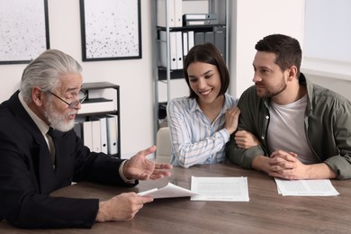 Young couple consulting insurance agent about pension plan at wooden table indoors