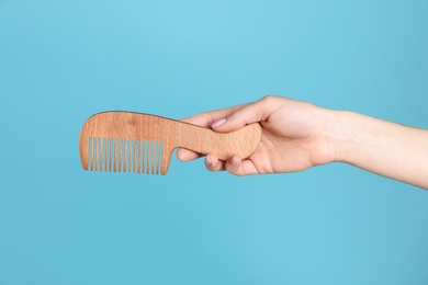 Photo of Woman holding wooden hair comb against blue background, closeup