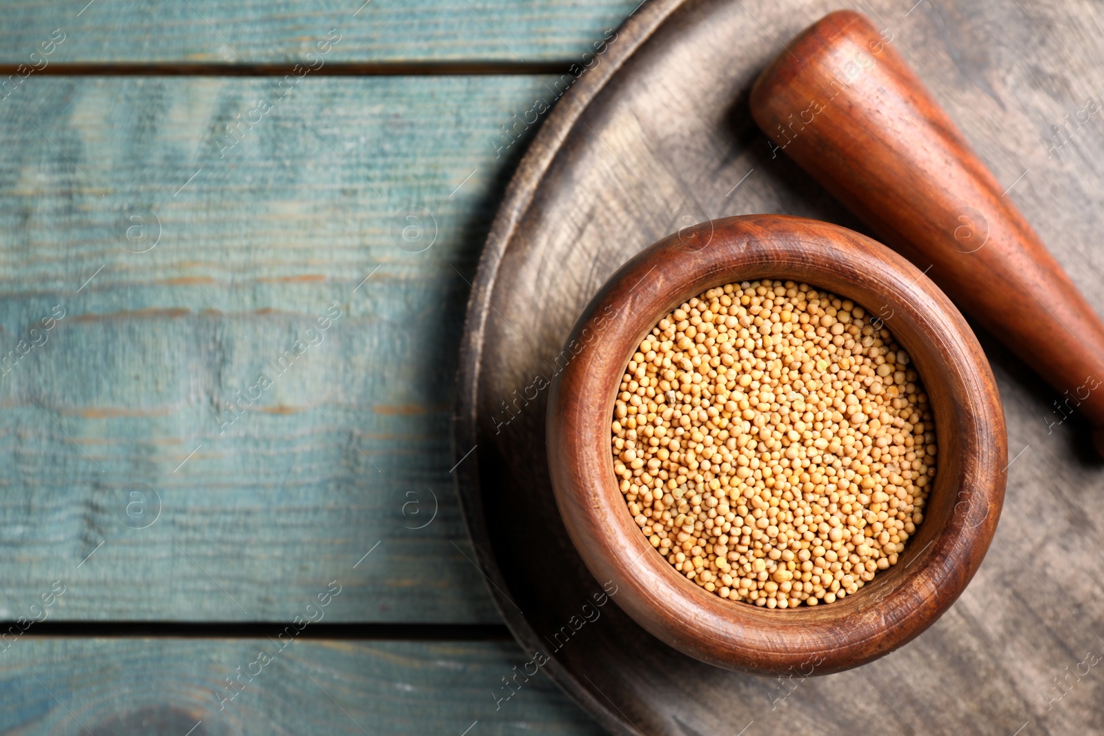 Photo of Pestle and mortar with mustard seeds on wooden table, flat lay. Space for text