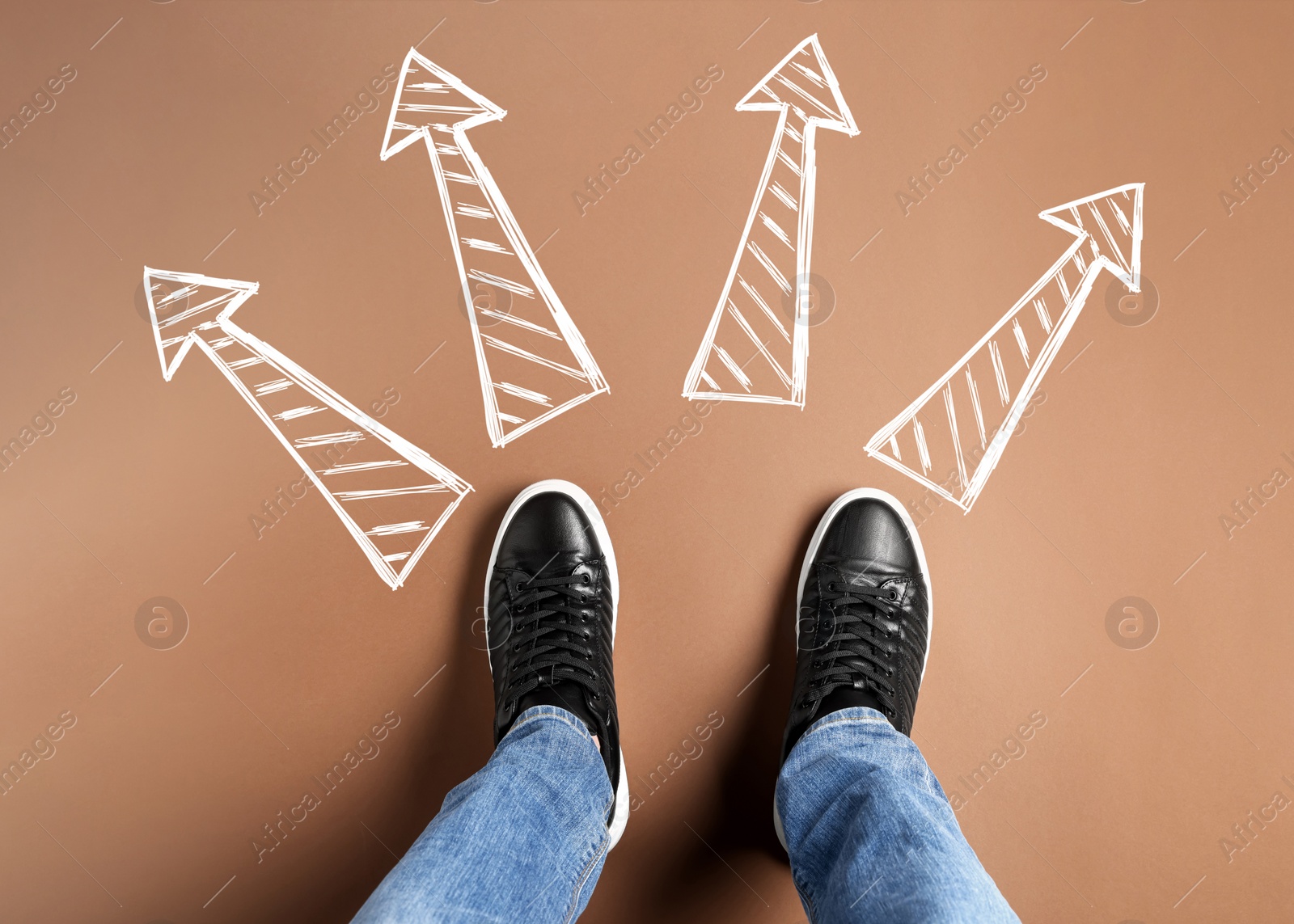 Image of Choosing future profession. Man standing in front of drawn signs on brown background, top view. Arrows pointing in different directions symbolizing diversity of opportunities