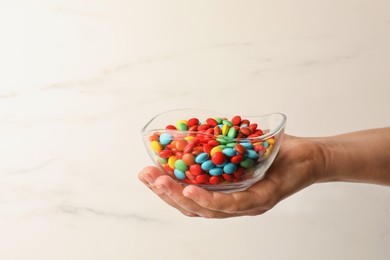 Photo of Woman with bowl of tasty colorful candies on white marble background, closeup. Space for text