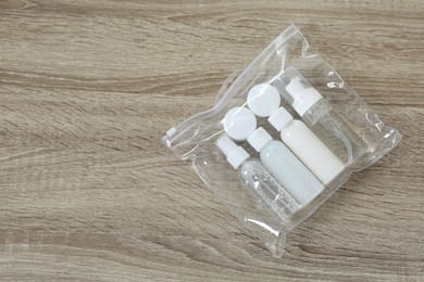 Photo of Cosmetic travel kit in plastic bag on wooden table, top view and space for text. Bath accessories