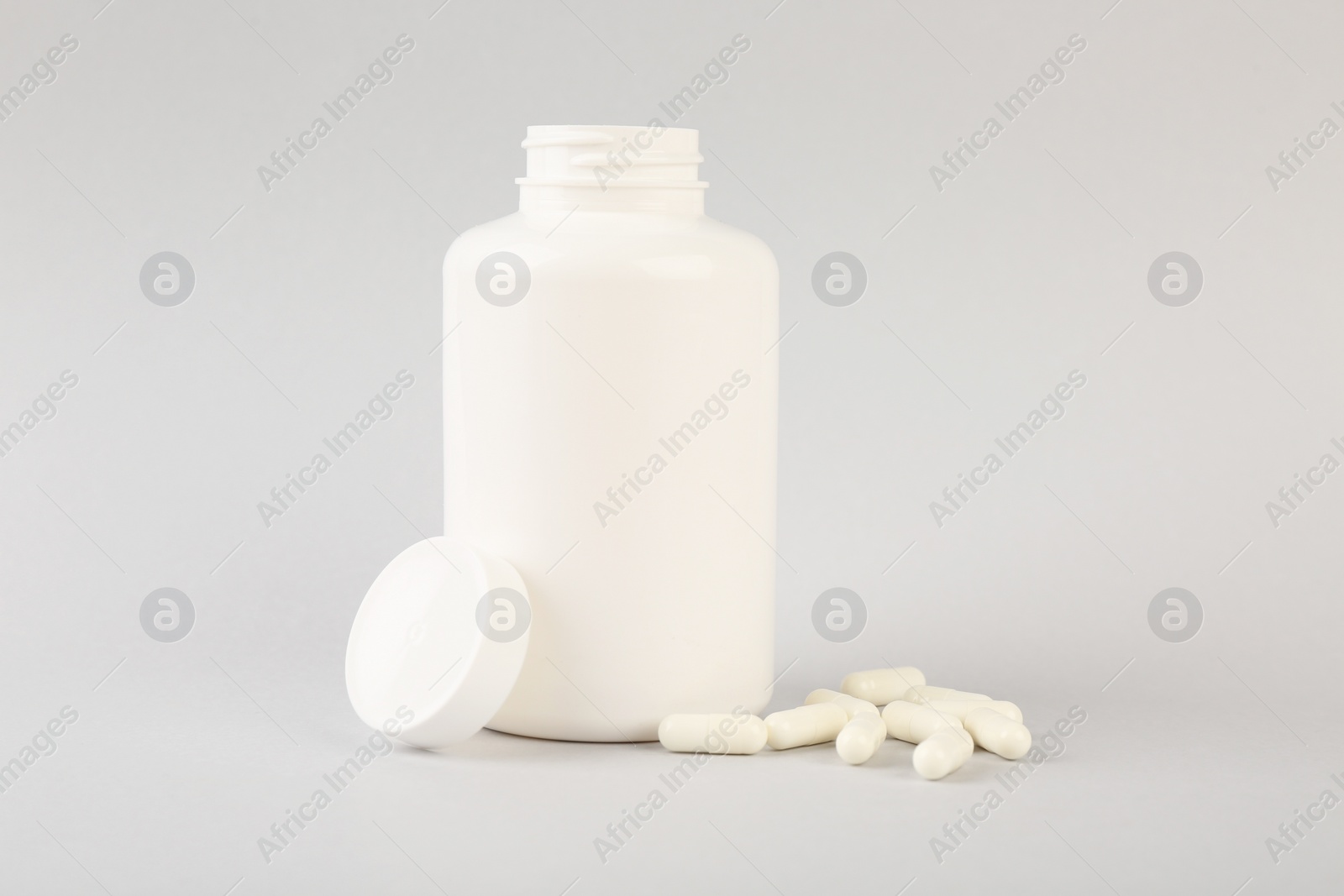 Photo of Blank white jar with vitamin capsules on light grey background, space for text