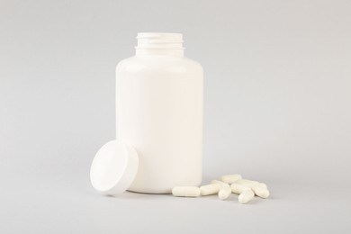 Photo of Blank white jar with vitamin capsules on light grey background, space for text