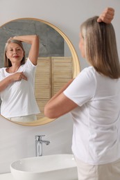 Beautiful senior woman doing breast self-examination near mirror in bathroom