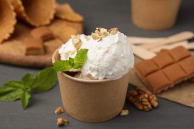 Photo of Tasty ice cream with mint and nuts in paper cup on grey table, closeup